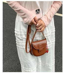 Brown vintage saddle bag with strawberry charm accessory worn by model on street