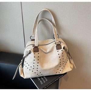 Detailed macro view of beige suede tote bag with metallic rivets on black sofa
