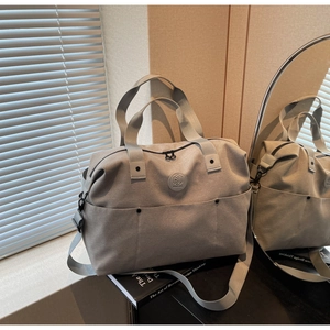 Detail of grey travel bag with circular logo, reinforced handles and side metal buckle