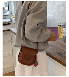 Close-up of vintage brown leather saddle bag with strawberry charm in minimalist setting
