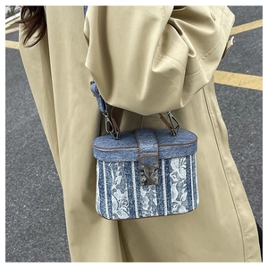 Lace-covered denim bucket bag styled with a beige trench coat for a chic urban look