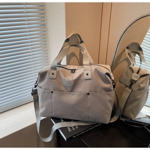 Detail of light grey canvas duffel bag with circular logo on black desk with book