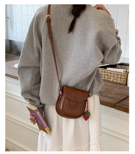 Detail of vintage brown saddle bag with strawberry charm in a minimalist interior