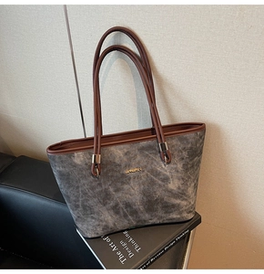 Detail of grey suede tote bag with brown leather handles and golden metal logo