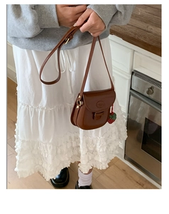 Close-up of retro brown saddle bag with a cute strawberry charm on a white skirt