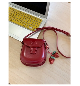 Close-up of vintage red saddle bag with strawberry charms on a desktop setting