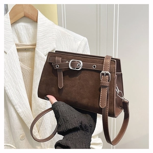 Détail d'un sac bandoulière en daim marron foncé avec boucle décorative et œillets argentés
