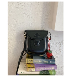 Detail of black mini saddle bag with matte leather finish and strawberry charm pendant