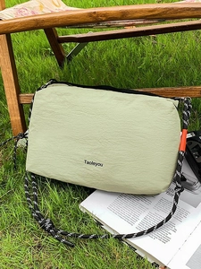 Light green outdoor crossbody bag with braided rope strap on natural grass background