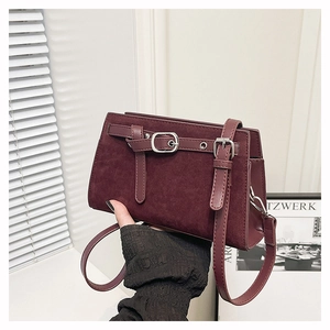 Détail d'un sac bandoulière bordeaux en daim mat avec boucles argentées à la main