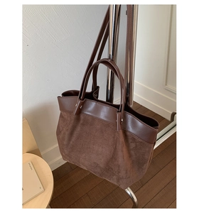 Detail of dark brown suede and leather tote bag featuring dual shoulder straps on a rack