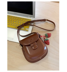Detailed top view of a dark brown vintage saddle bag with strawberry charms on a desk