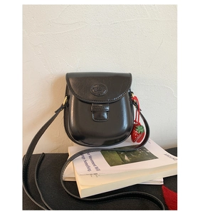 Detailed macro view of black saddle bag flap with London logo and strawberry charm detail