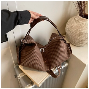 Close-up of brown plaid tote bag with wide leather handle on a silver suitcase