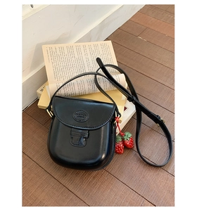 Detail of black leather saddle bag with strawberry charms on vintage books background