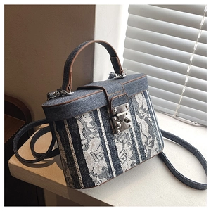 Detail of blue denim and white lace stitching on a rigid box-shaped crossbody handbag