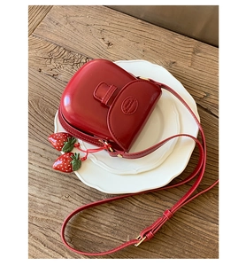 Detail view of mini red saddle bag with strawberry charms and embossed logo texture
