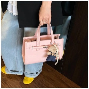Detail view of pink leather handbag featuring a pebble grain texture and a bear charm