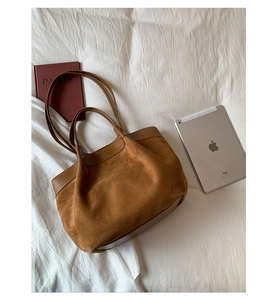 Top-down view of a large brown suede tote bag with leather straps on a white fabric background