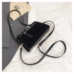 Détail du sac noir en velours et cuir avec boucle métallique argentée sur tissu blanc