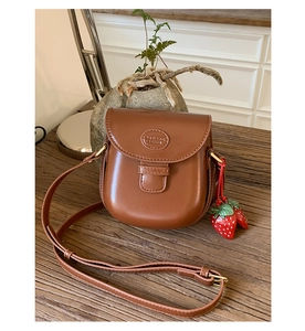 Close-up of brown vintage saddle bag with strawberry charms on a wooden table