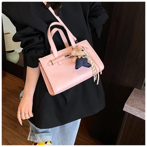 Close-up of pink litchi grain leather handbag with metal lock and cute teddy bear charm