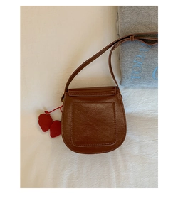 Detail of a brown saddle bag with a back pocket and two red heart charms on the strap