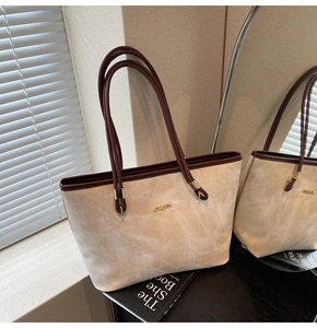 Detailed macro view of beige tote bag with golden metal logo on textured faux suede