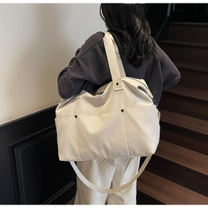 Close-up of cream canvas travel tote bag with leather logo patch and adjustable straps