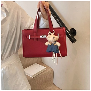Detail of red leather tote bag featuring a metal twist lock and a cute bear charm