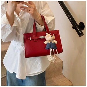 Close-up of burgundy leather handbag with litchi texture and cute bear charm detail