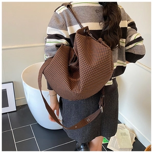 Detailed side view of large brown plaid crossbody bag with orange logo embroidery