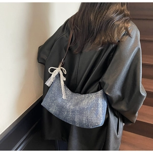 Detail der blauen Denim Hobo-Tasche mit weißer Spitzenschleife und Perlenanhänger