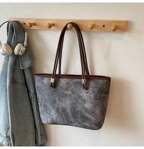 Detail of grey tote bag featuring matte texture, brown straps and gold metal logo