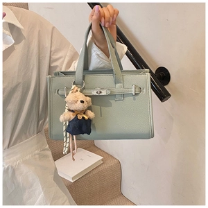 Detail of mint green lychee grain leather handbag with classic metal clasp and teddy bear charm