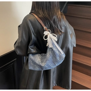 Detail der Hobo-Tasche mit weißer Spitzenschleife und Perlenanhänger auf blauem Denim