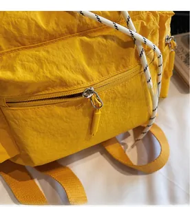 Macro view of smooth zipper and textured woven drawstring on yellow nylon backpack