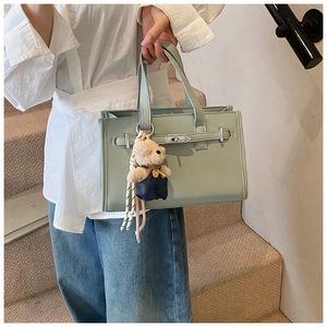 Detail of mint green square handbag with silver clasp and plush bear charm on strap