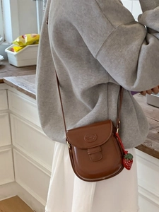Vintage brown saddle crossbody bag with a strawberry pendant in a cozy kitchen setting