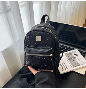 Detail of a black mini backpack with silver rivets placed on a stylish black leather chair