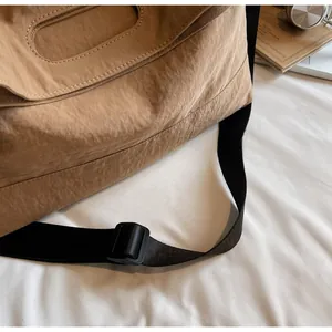 Detail of adjustable black wide strap on brown nylon crossbody tote bag with buckle