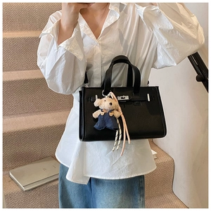 Detail of black lychee leather handbag with silver lock and cute bear plush charm