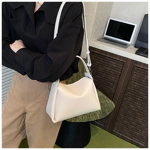 Chic cream-colored crossbody bag in pebble grain leather worn over a woman's shoulder