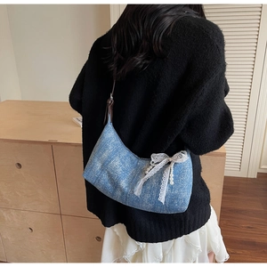 Detail der blauen Denim-Halbmondtasche mit weißer Spitzenschleife und Perlenanhänger