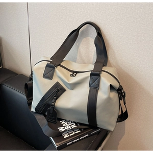 Detail of light grey travel bag with black handles and shoulder strap on leather surface