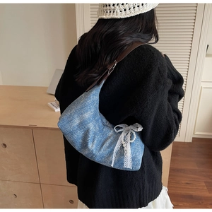 Detail der blauen Hobo-Tasche mit weißer Spitzenschleife, Perlenanhänger und Lederriemen