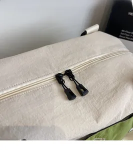 Detail of smooth two-way zippers with rope pulls on the beige nylon travel bag