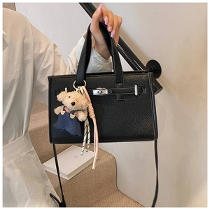 Detail of black pebbled leather tote bag with silver turn-lock and teddy bear charm