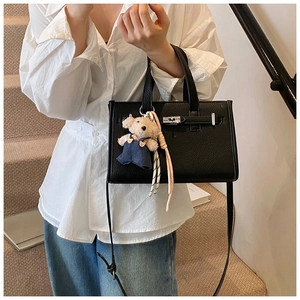 Detail view of black litchi pattern leather handbag with silver clasp and bear charm