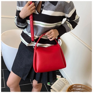 Sac bandoulière en cuir rouge grainé porté par un mannequin en pull à rayures
